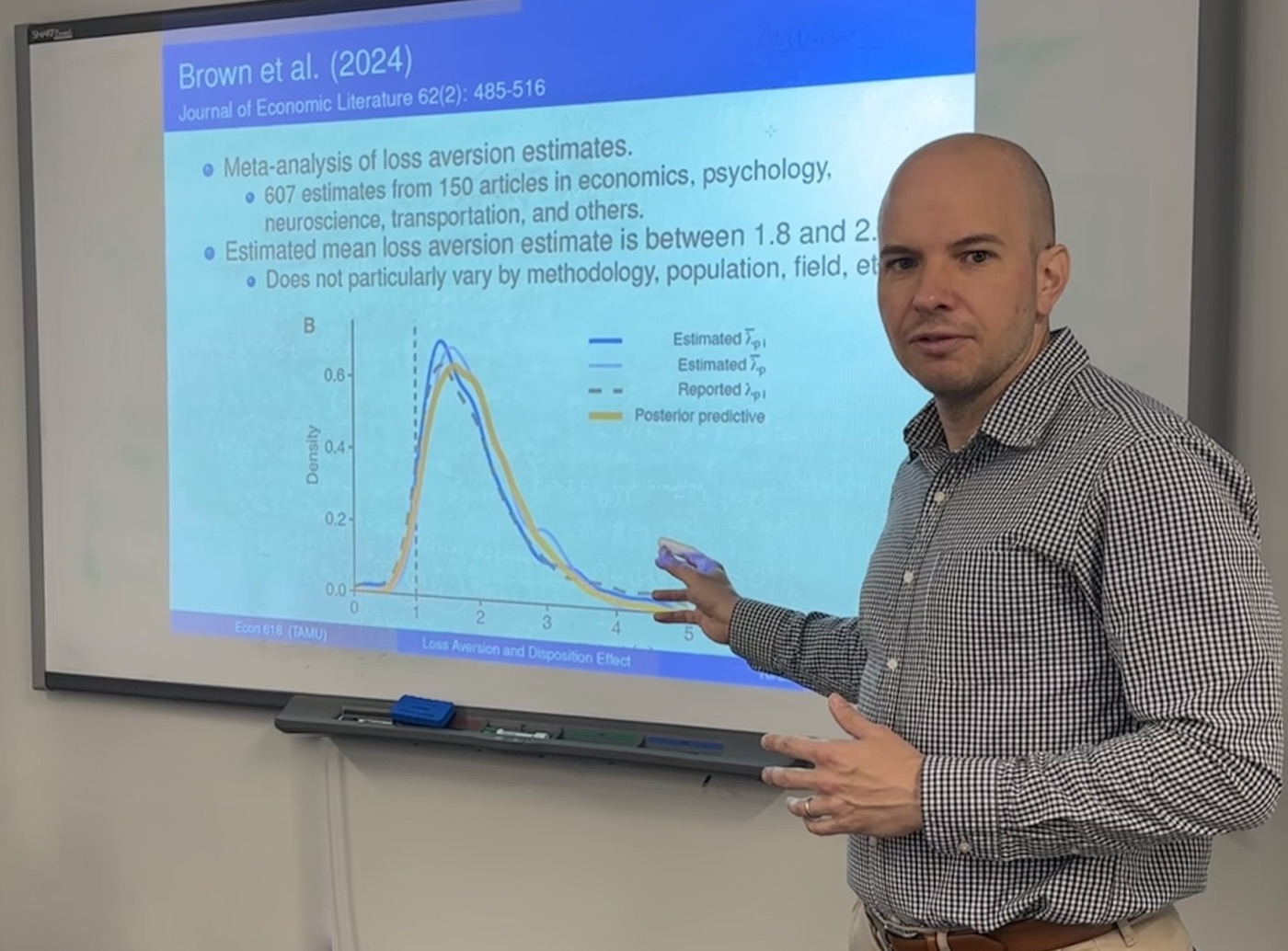Alexander L. Brown teaching, pointing at a slide of his loss aversion meta-analysis